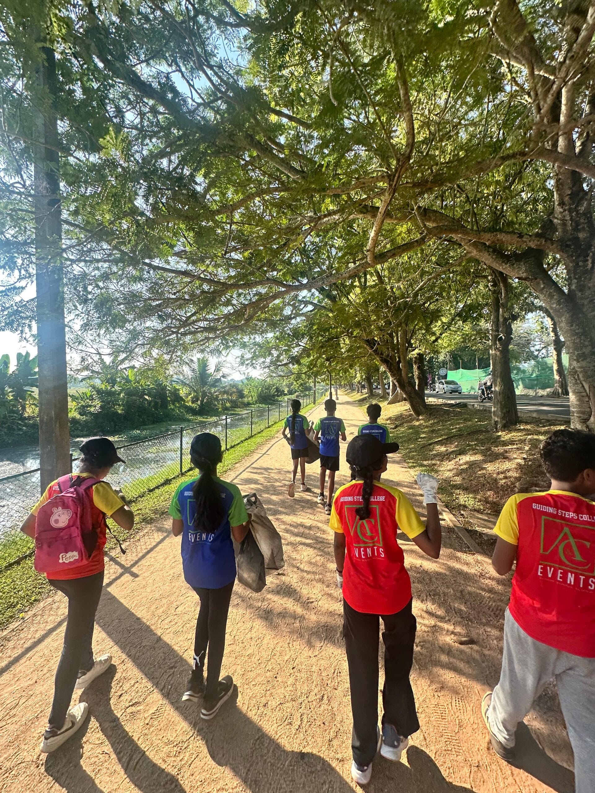 Guiding Steps College students walking a tree-lined lakeside track collecting litter during a clean-up event