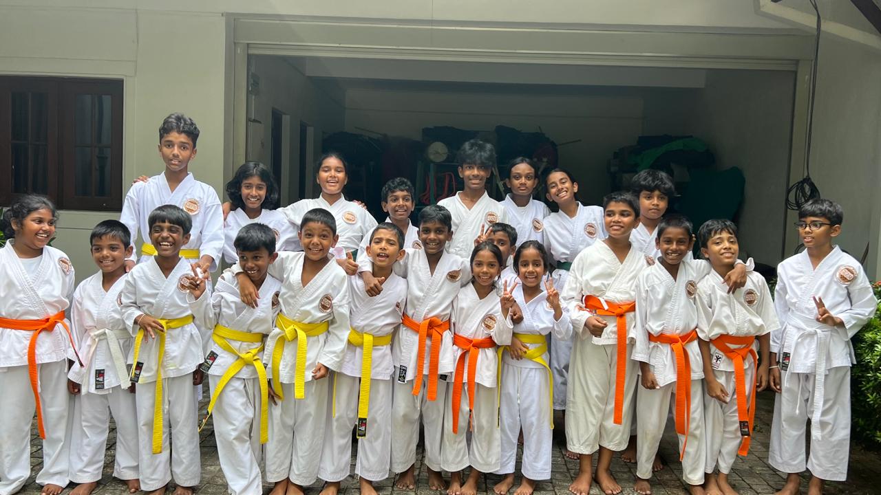 Karate students at Guiding Steps College smiling in white uniforms with yellow, orange and white belts