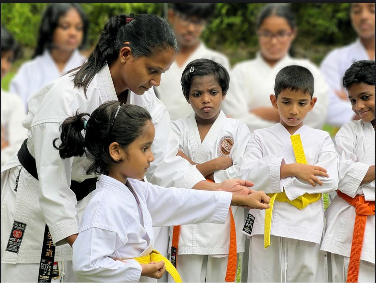 Karate instructor guiding a young student's punching technique while classmates watch
