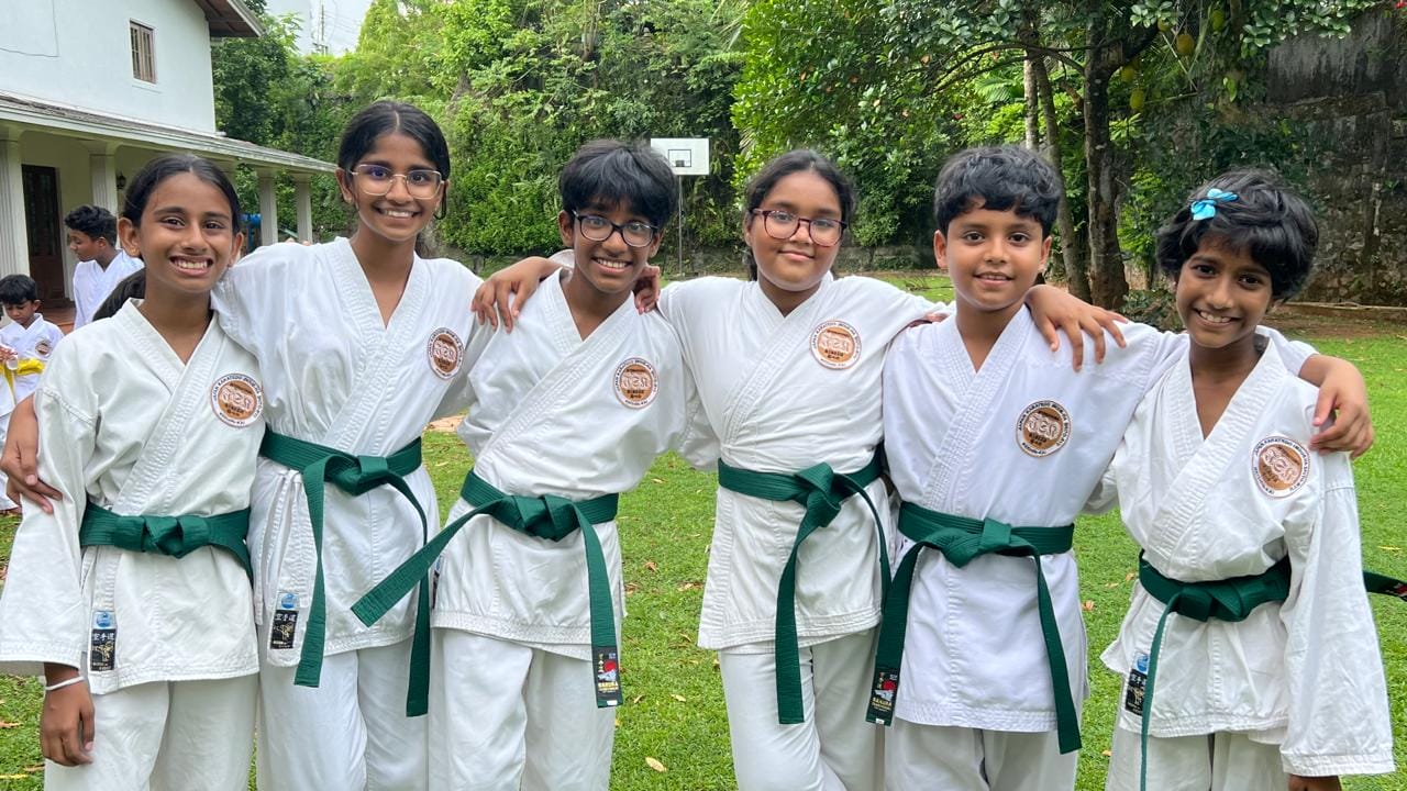 Six smiling green belt karate students standing arm in arm after training