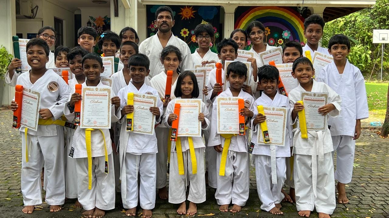 Karate students holding grading certificates and new belts with their instructor at Guiding Steps College